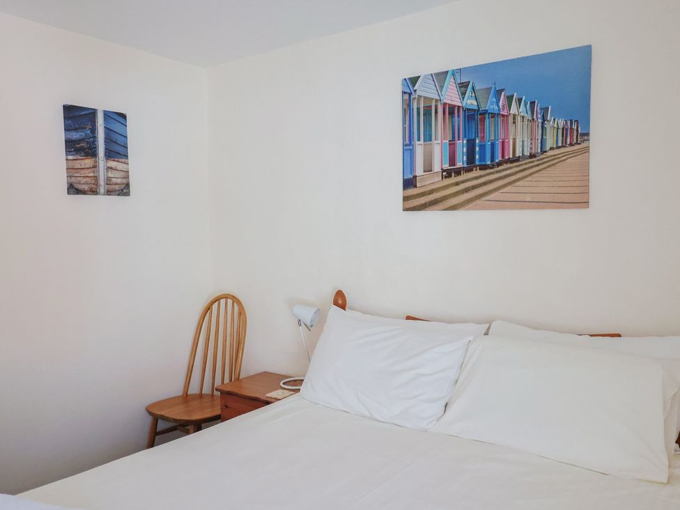 A bedroom with a bed, side table, chair and wall art at 3 Dolphin Cottages in Lyme Regis