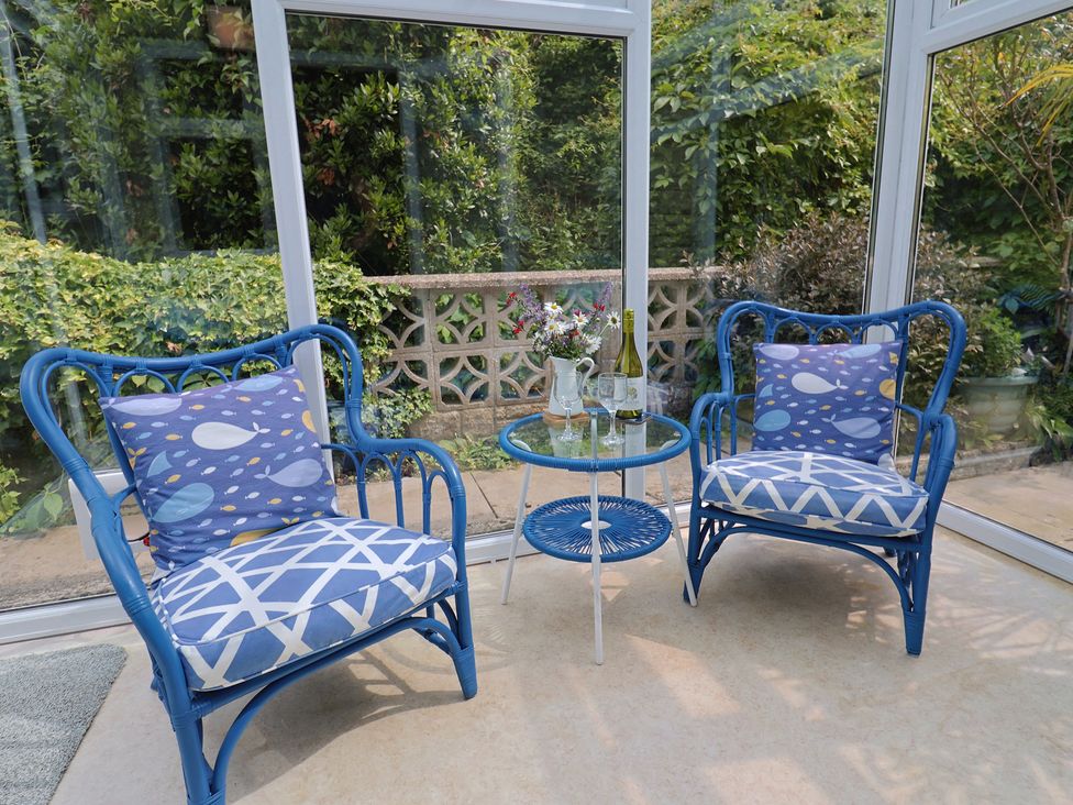 A conservatory with two rattan chairs and a table at High Trees in Lyme Regis