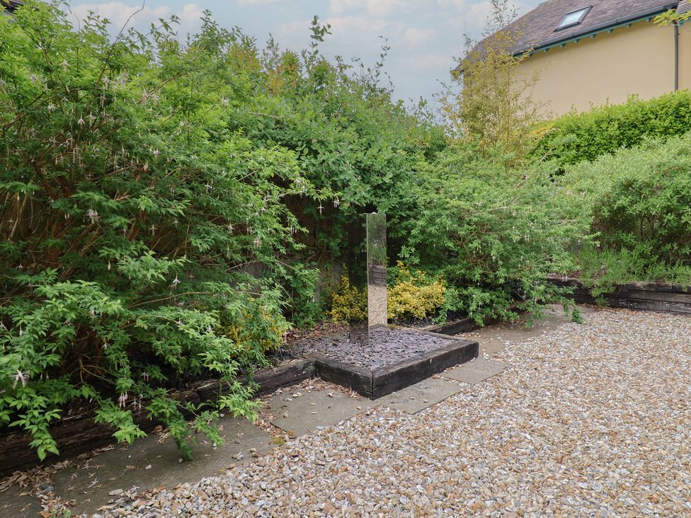 A garden with a metal sculpture surrounded by bushes and gravel at Yard Cottage in Rousdon