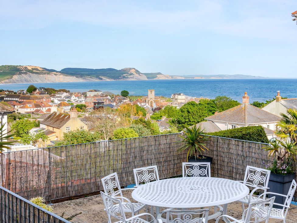 An outdoor dining area with table and chairs overlooking the sea and hills at 2 Hadleigh Villas Lyme Regis