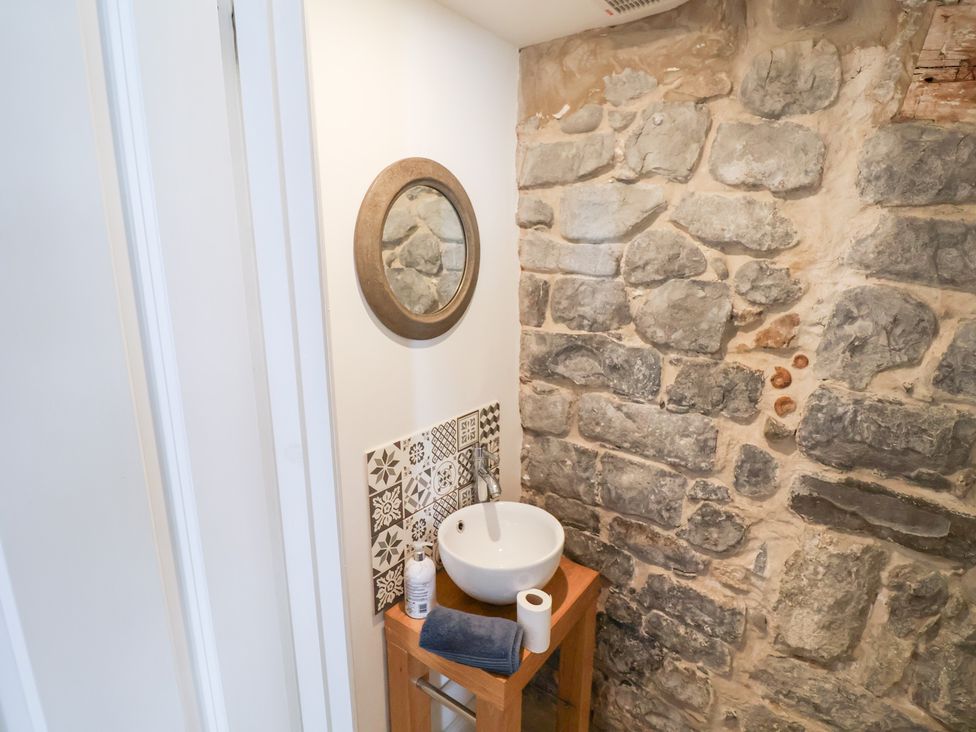 A bathroom with a sink, mirror, wooden table, and stone wall at The Bakehouse in Lyme Regis