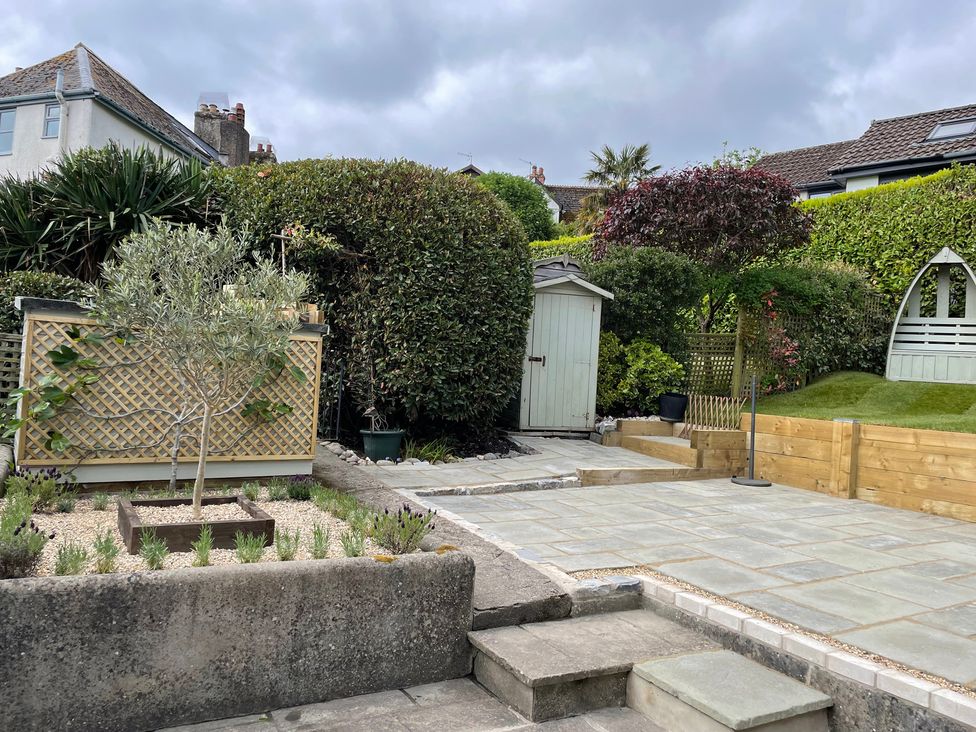 A garden with a shed, olive tree, and patio stones at The Bakehouse Lyme Regis
