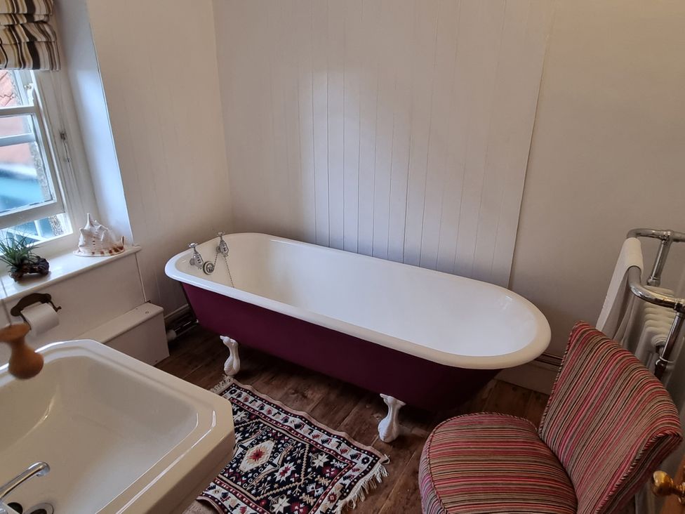 A bathroom with a bathtub, sink and chair at Old Monmouth in Lyme Regis