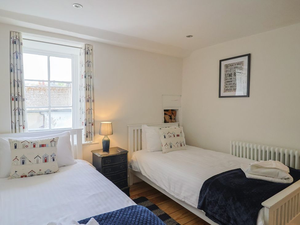 A bedroom with two beds, a lamp, and a window at The Little Rose in Lyme Regis