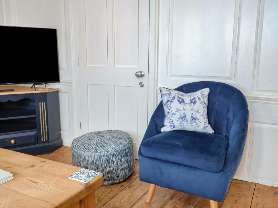 A living room with a blue armchair and a television at The Little Rose in Lyme Regis