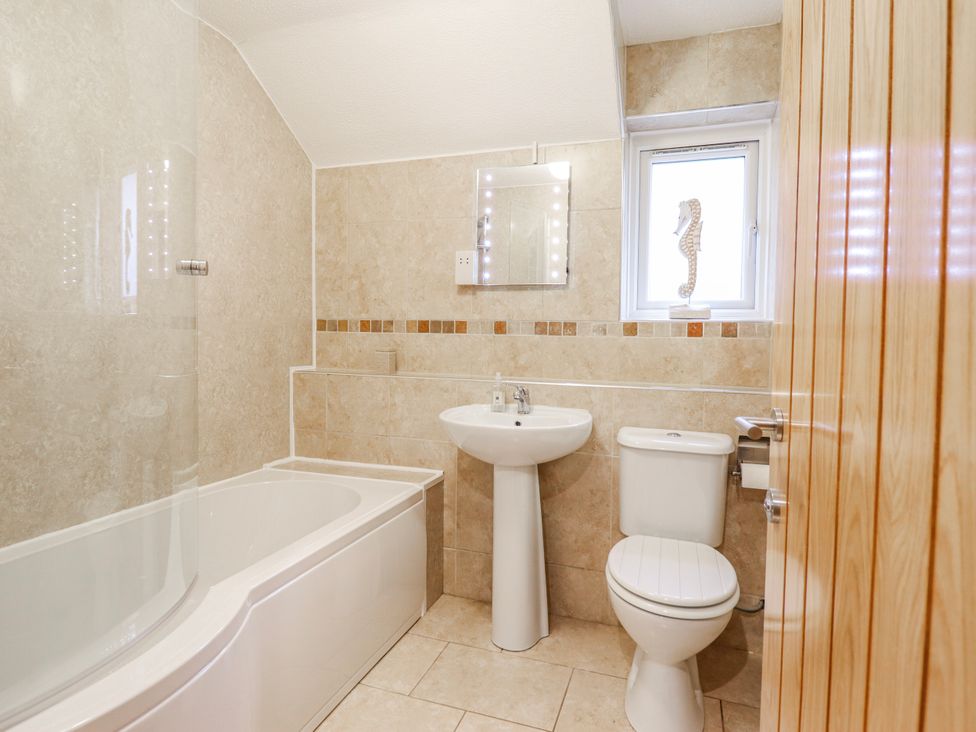 A bathroom with bathtub, toilet, sink, and mirror at Green Cottage Borth-Y-Gest