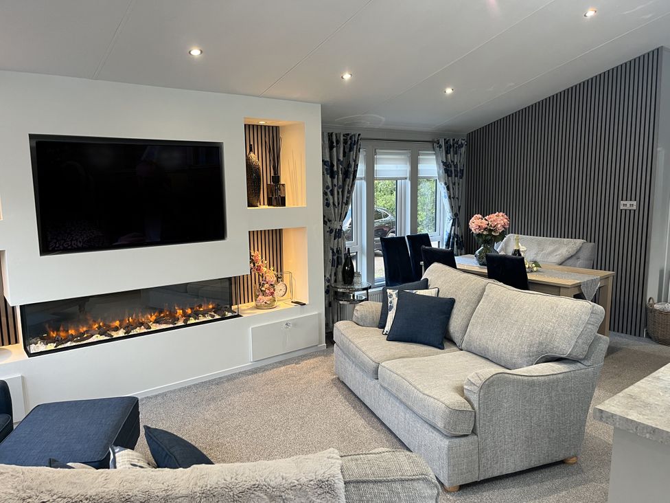 A living room with a fireplace and dining table at Loluke Lodge on The Lake 5 Coniston Drive, Borwick near Carnforth