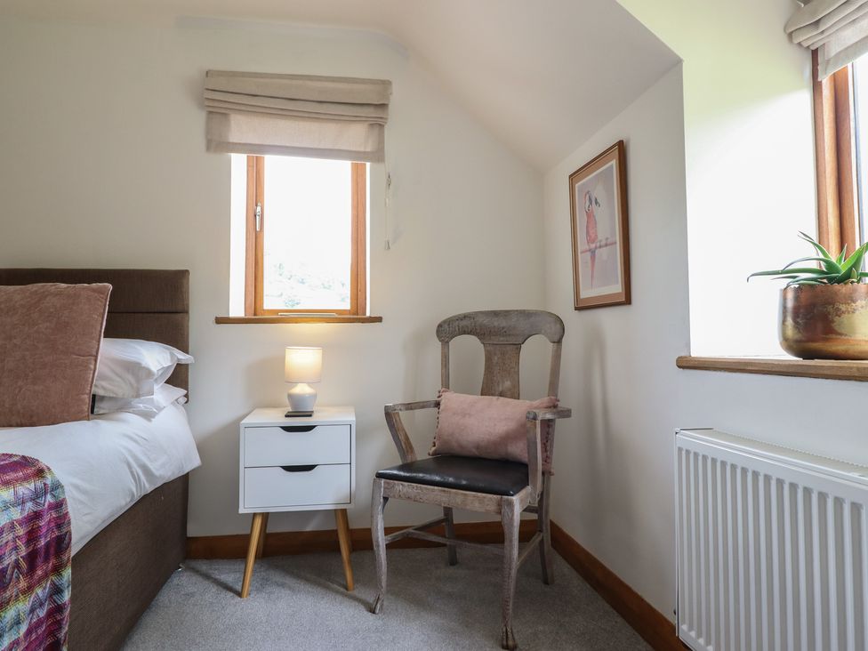 A bedroom with a bed, nightstand, chair, and window at Cwmwr in Penybontfawr