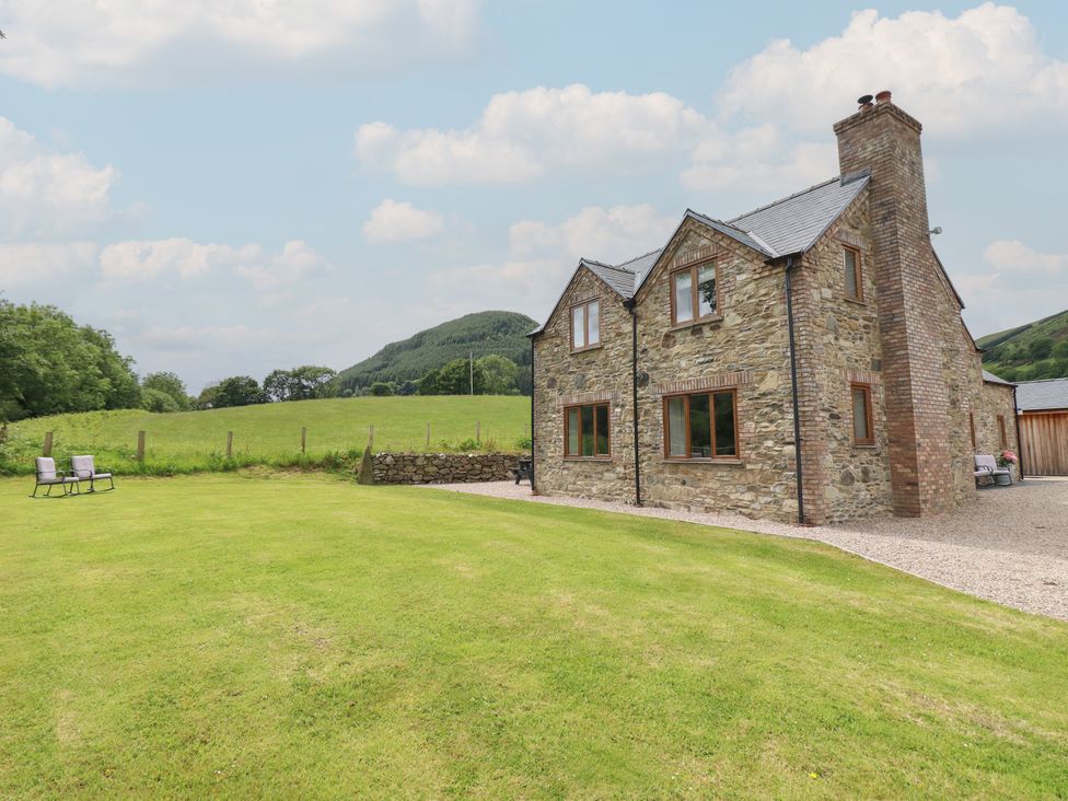 A stone house with a lawn and mountains at Cwmwr in Penybontfawr
