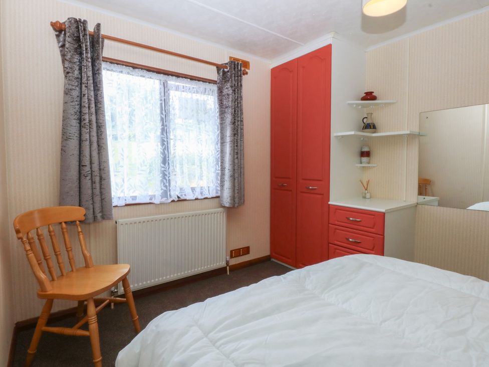 A bedroom with a bed, chair, wardrobe, and window at 16 Forest Lodge in Chwilog