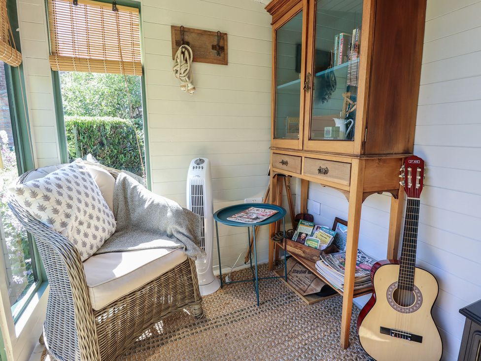 A sunroom with a chair, table, bookshelf, fan and guitar at Hangmans cottage in Horncastle