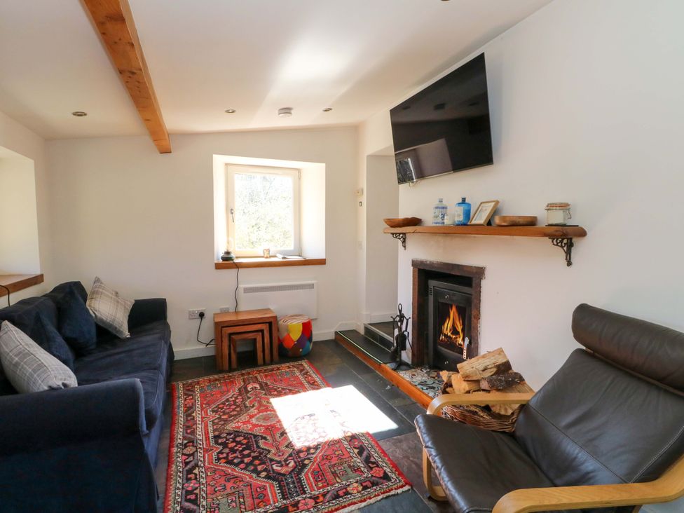 A living room with a sofa, armchair, and fireplace at Gun Powder Cottage in Tighnabruaich