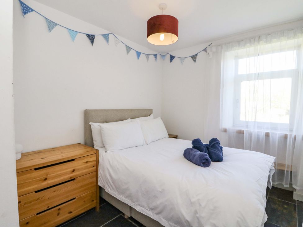 A bedroom with a bed, dresser, and bunting at Gun Powder Cottage in Tighnabruaich
