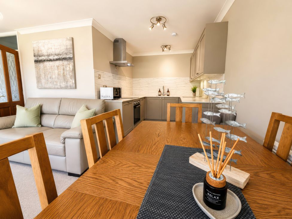 A dining room with a dining table and kitchen in view at 6 Coedrath Park - Swn y Mor in Saundersfoot