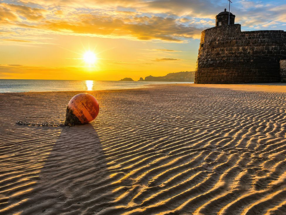 A buoy on the beach with a fort at sunset at 6 Coedrath Park - Swn y Mor in Saundersfoot
