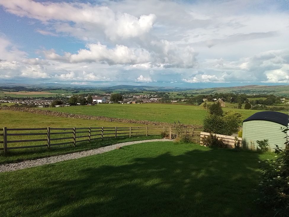 A garden view with grass, fence, trees, and hills at The Journeyman Luxury Shepherds Hut Barnoldswick