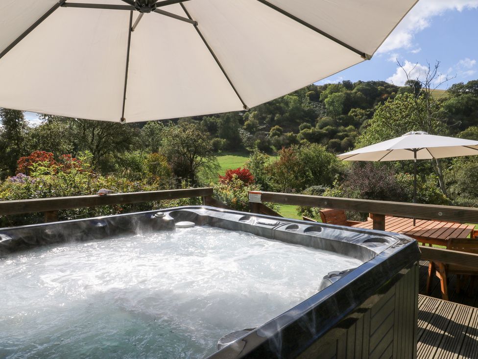 A hot tub with patio umbrellas and seating in an outdoor area at Penarth in Cregrina near Builth Wells