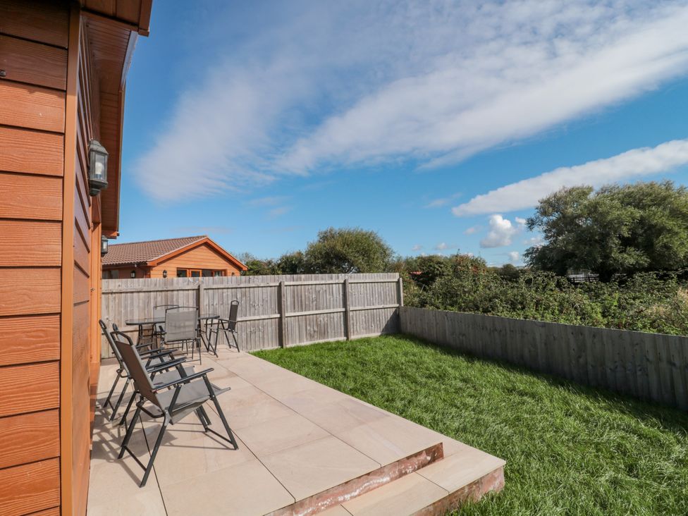 An outdoor patio area with chairs and a garden at Delphine Lodge, Meadow View Lodges Brean