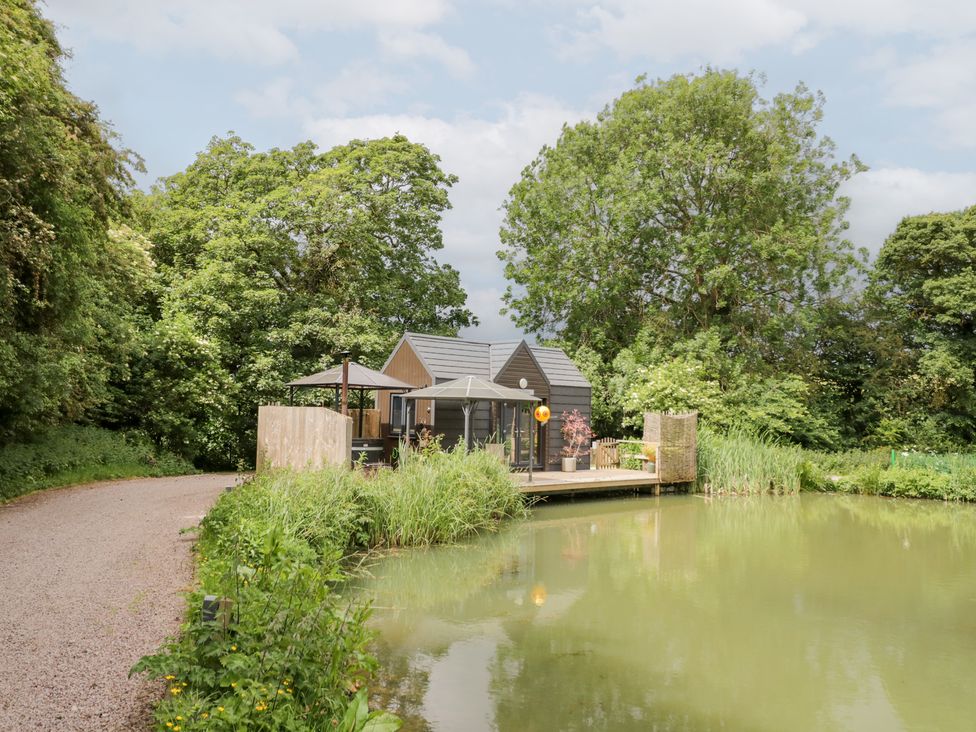 An outdoor area with a house by a pond at Maple Lodge at Bridge Lake Farm & Fishery Chacombe
