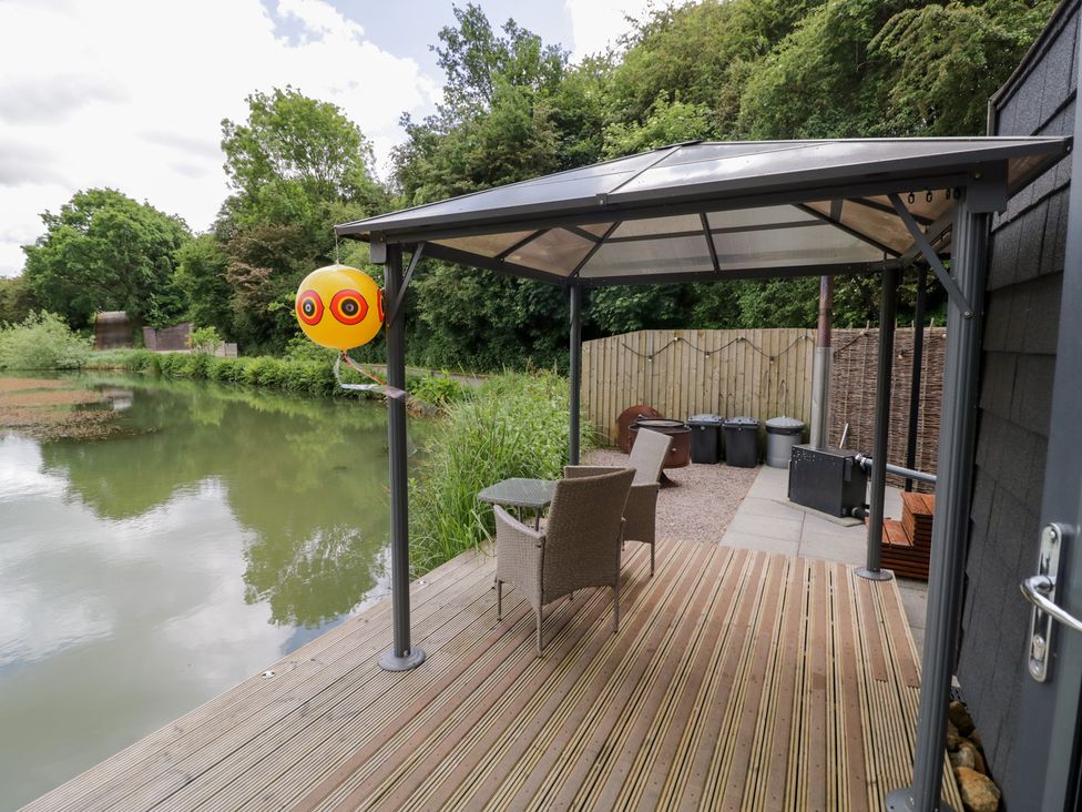 A patio area with chairs and a table near a pond at Maple Lodge at Bridge Lake Farm & Fishery Chacombe