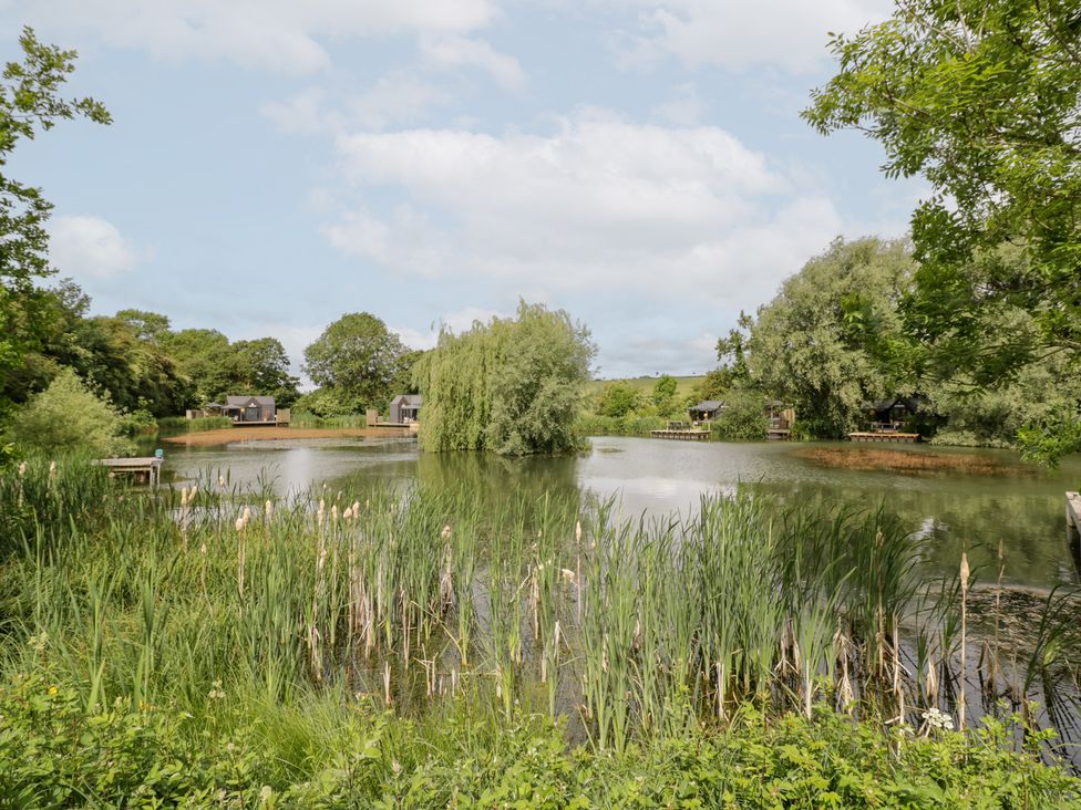 A view of a lake surrounded by trees and houses at Maple Lodge at Bridge Lake Farm & Fishery Chacombe