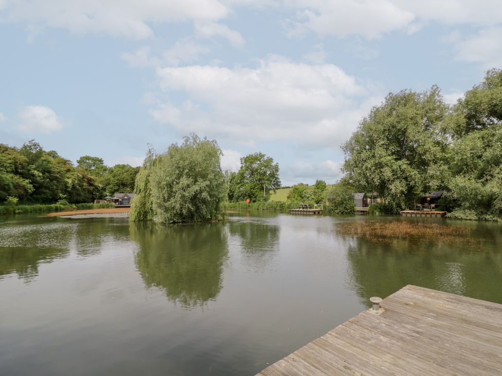 View of a lake with trees and fishing huts at Maple Lodge at Bridge Lake Farm & Fishery, Chacombe