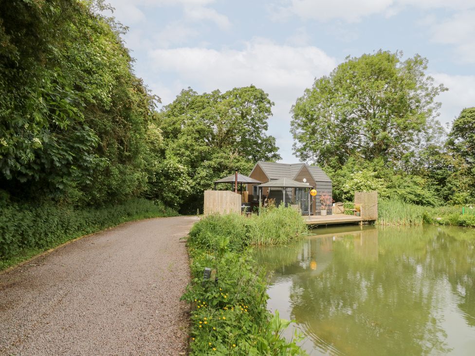 A cabin by a lake surrounded by trees at Maple Lodge at Bridge Lake Farm & Fishery Chacombe