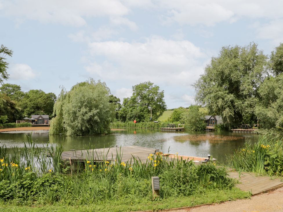 A pond surrounded by trees and benches at Maple Lodge at Bridge Lake Farm & Fishery, Chacombe