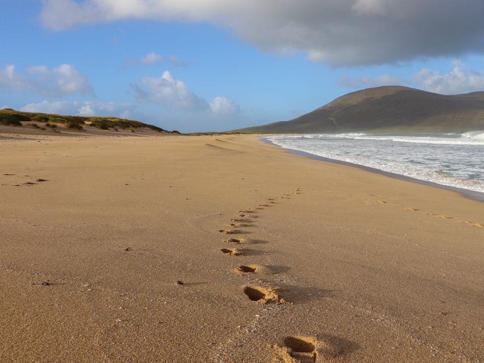 A beach with footprints in the sand and waves at Otter Cottage Scarista near Leverburgh