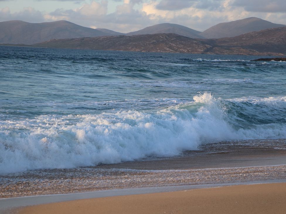 A beach with waves and mountains in the background at Otter Cottage Scarista near Leverburgh
