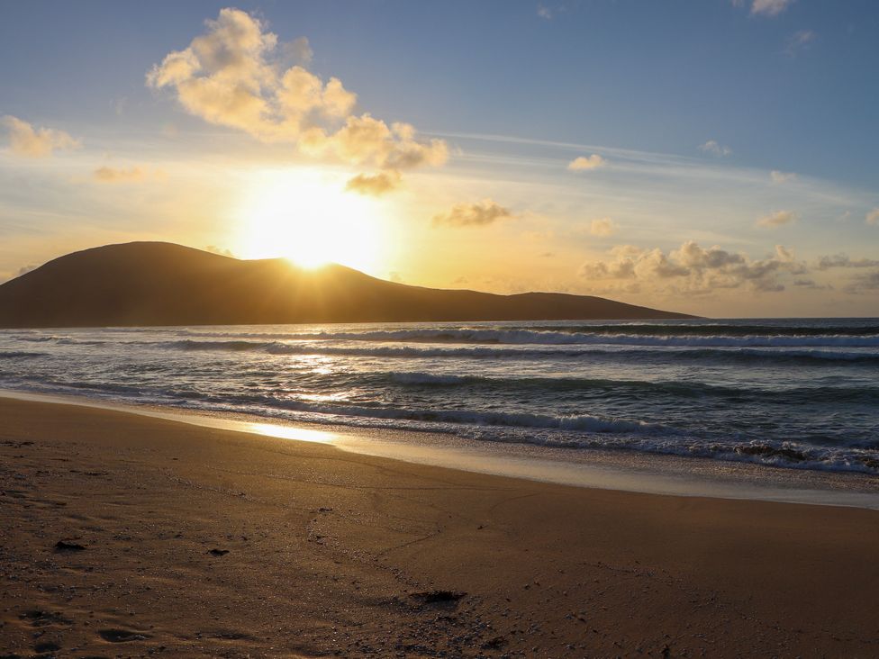 A beach with waves and a mountain during sunset at Otter Cottage in Scarista near Leverburgh