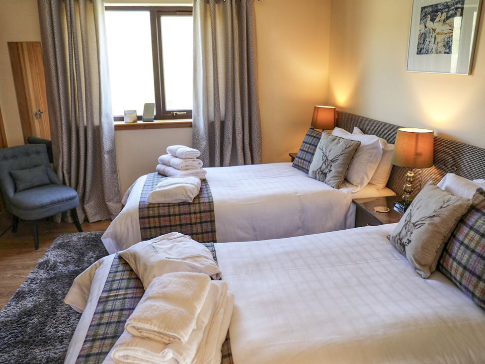 A bedroom with two beds and a chair at Corncrake Cottage in Leverburgh
