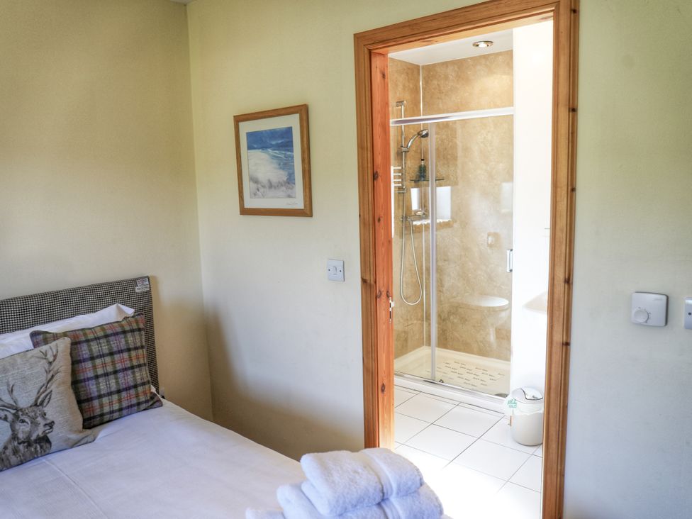 A bedroom with a bed and a bathroom with shower at Corncrake Cottage Leverburgh