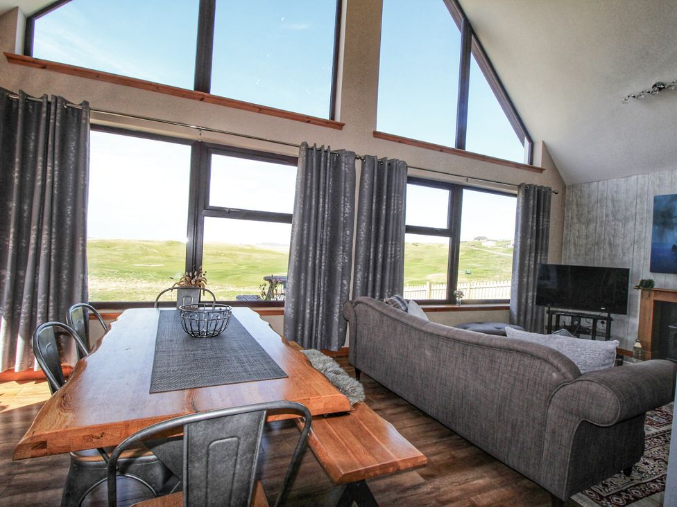 A living room with large windows and a dining table at Corncrake Cottage in Leverburgh
