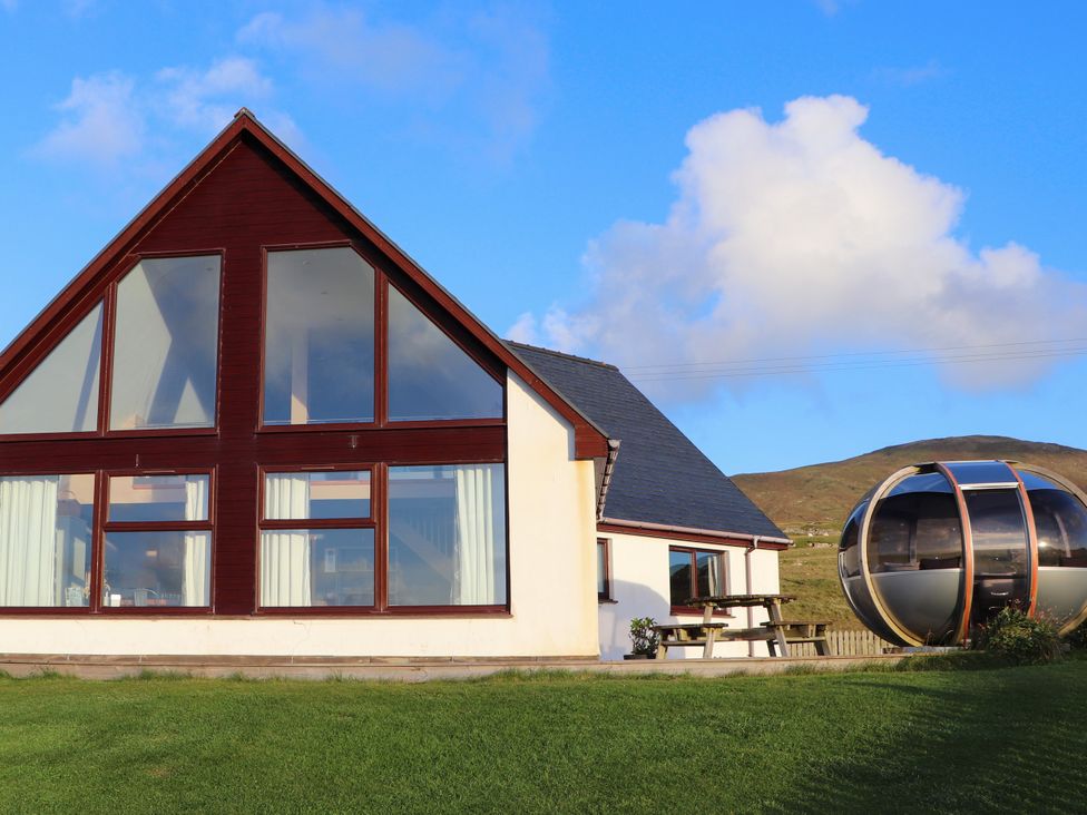 A house with large windows and a unique structure at Corncrake Cottage in Leverburgh