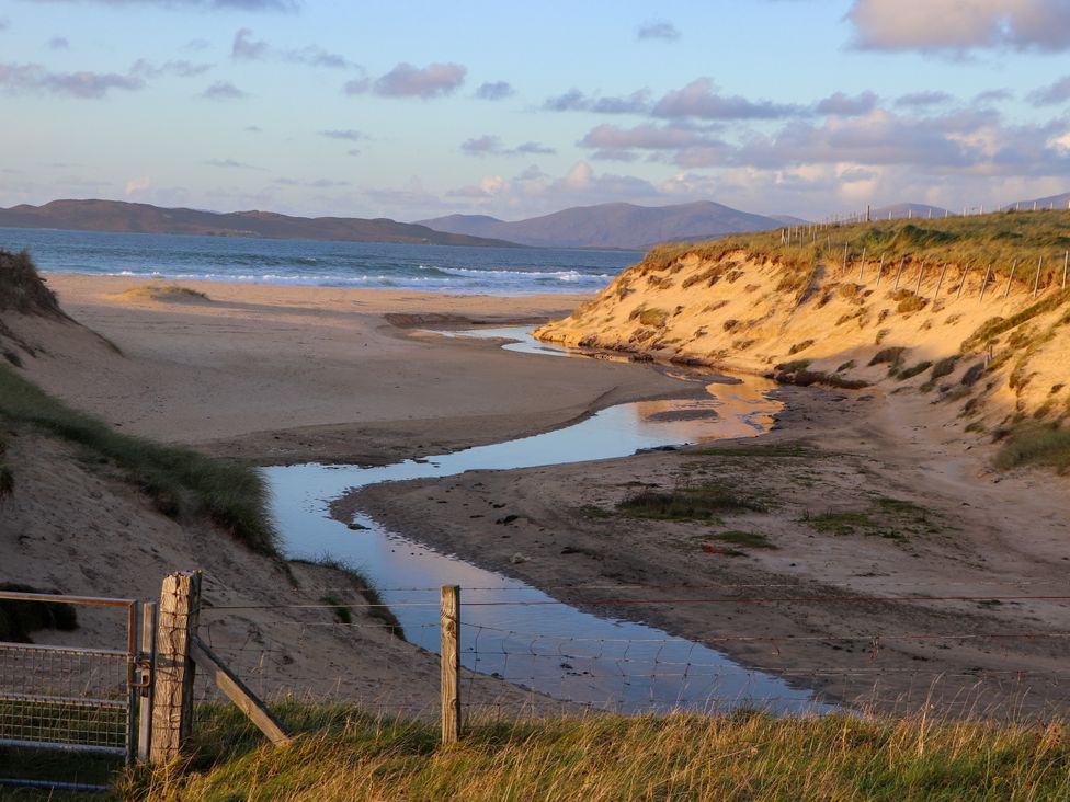 A beach scene with a stream flowing towards the sea at Corncrake Cottage in Leverburgh