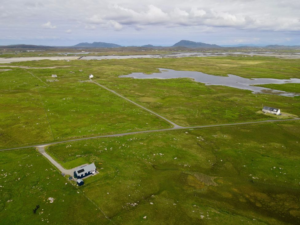 An aerial view of houses and fields near a body of water at Taigh Gorm Baleshare near Balivanich