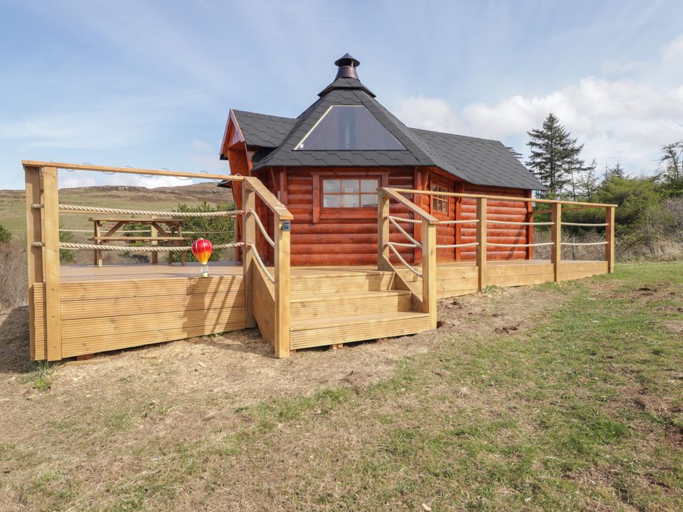 A log cabin with a wooden deck and railing at Falls Cottage in Uig