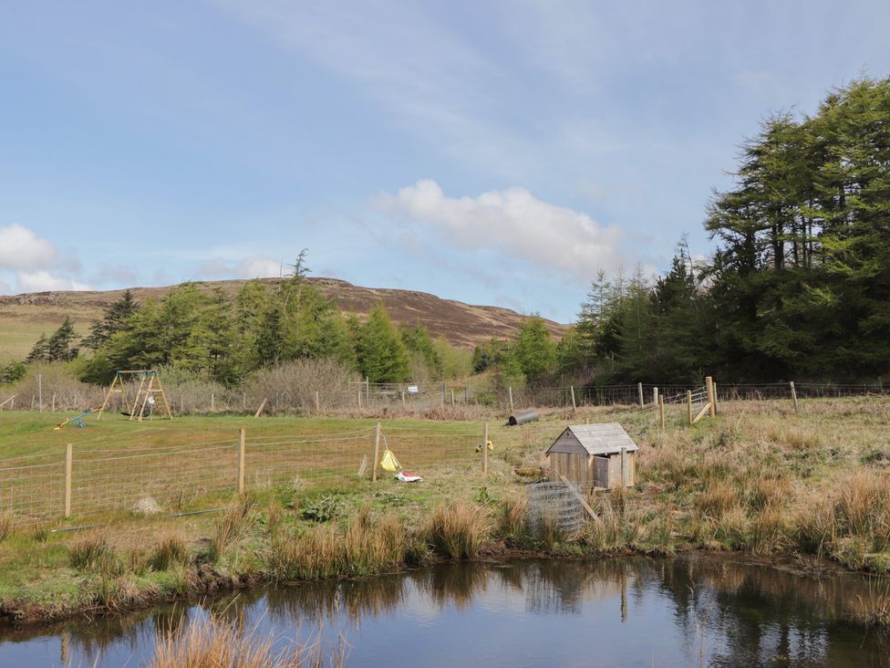 An outdoor area with a pond, playground equipment and a wooden shed at Falls Cottage in Uig