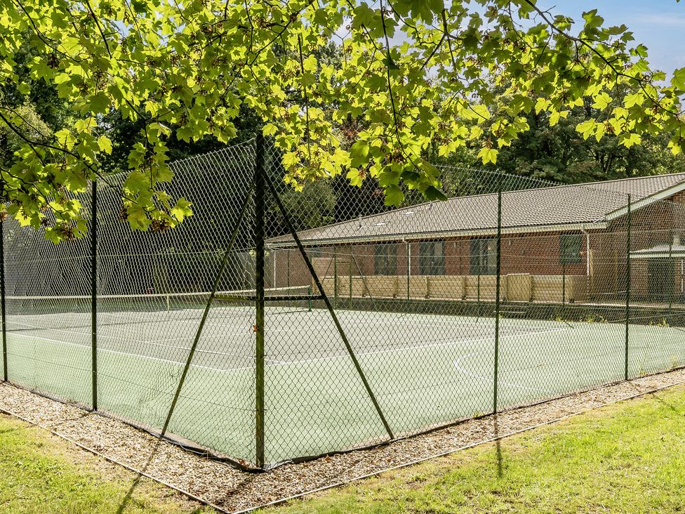 A tennis court enclosed by a fence with a building in the background at The Cottage in Wimborne Minster