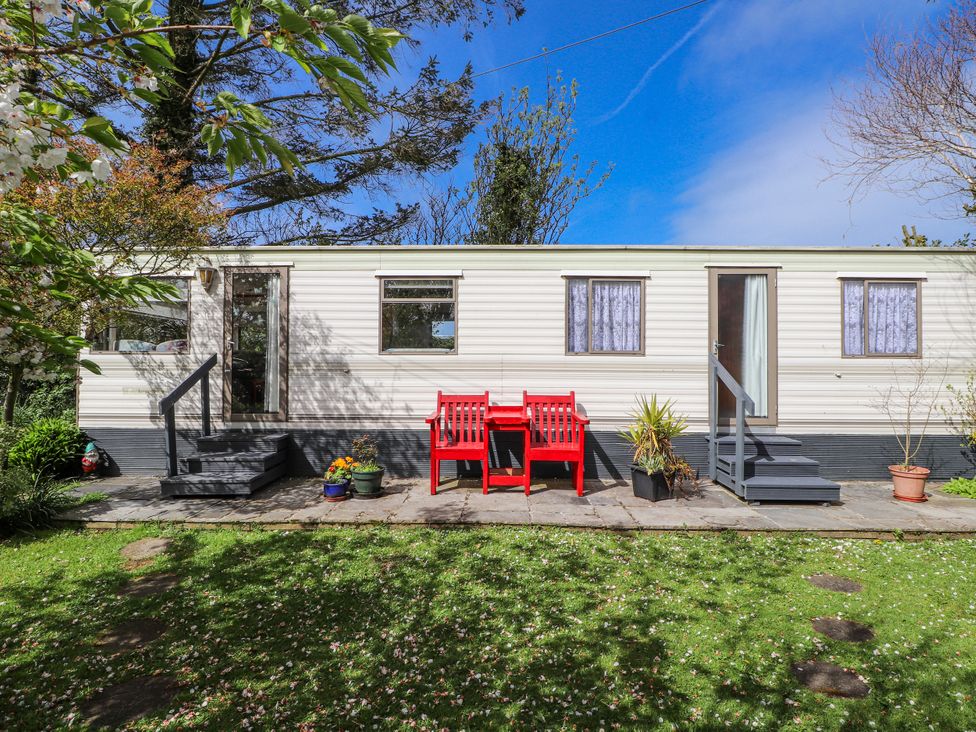 A caravan with red chairs and table in an outdoor space at Fron Dderw Caravan Llanfairynghornwy near Llanfechell