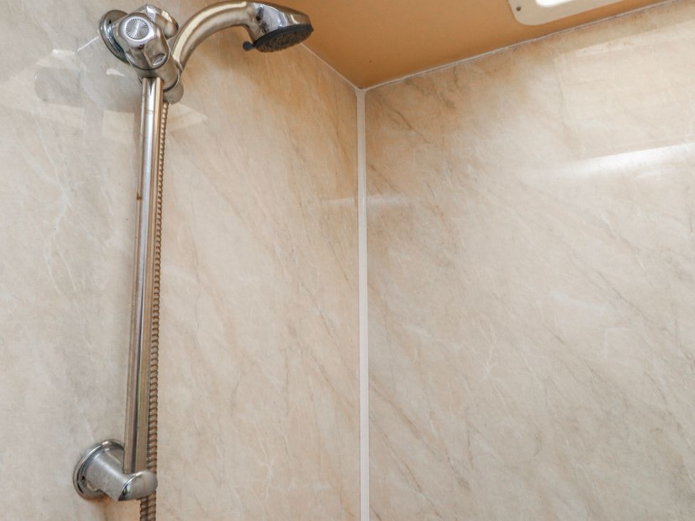 A shower with a shower head and tiled walls at Fron Dderw Caravan Llanfairynghornwy near Llanfechell