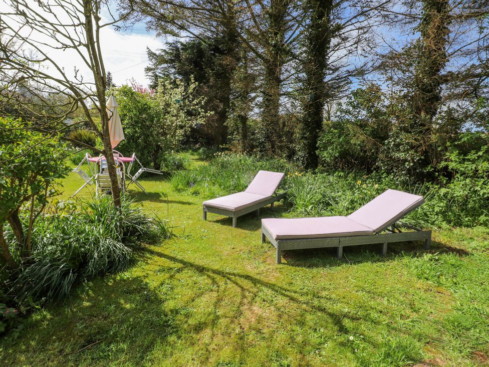 A garden with lounge chairs and an umbrella at Fron Dderw Caravan in Llanfairynghornwy near Llanfechell