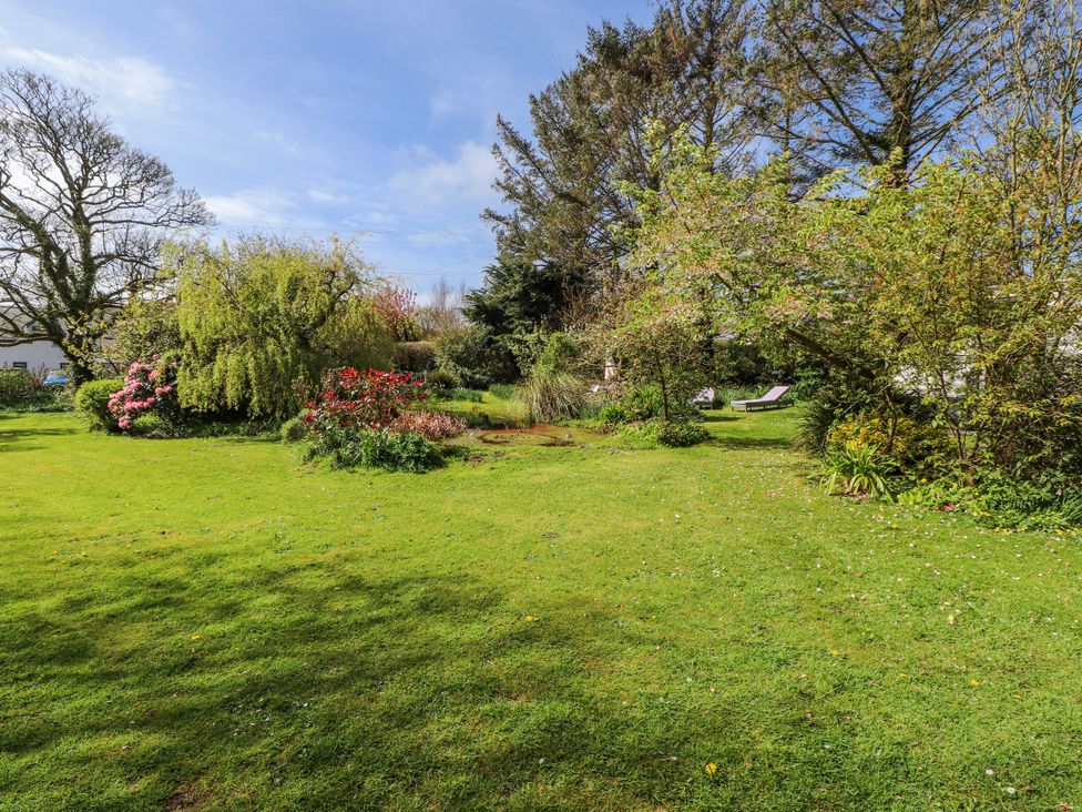 A garden with trees, flowers, grass, and a pond at Fron Dderw Caravan, Llanfairynghornwy near Llanfechell