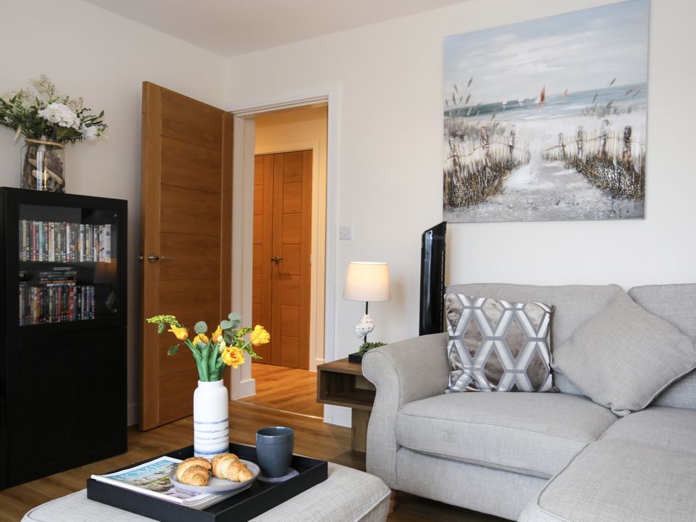 A living room with a sofa, flower vase, and DVD shelf at Apartment 3 in Trearddur Bay