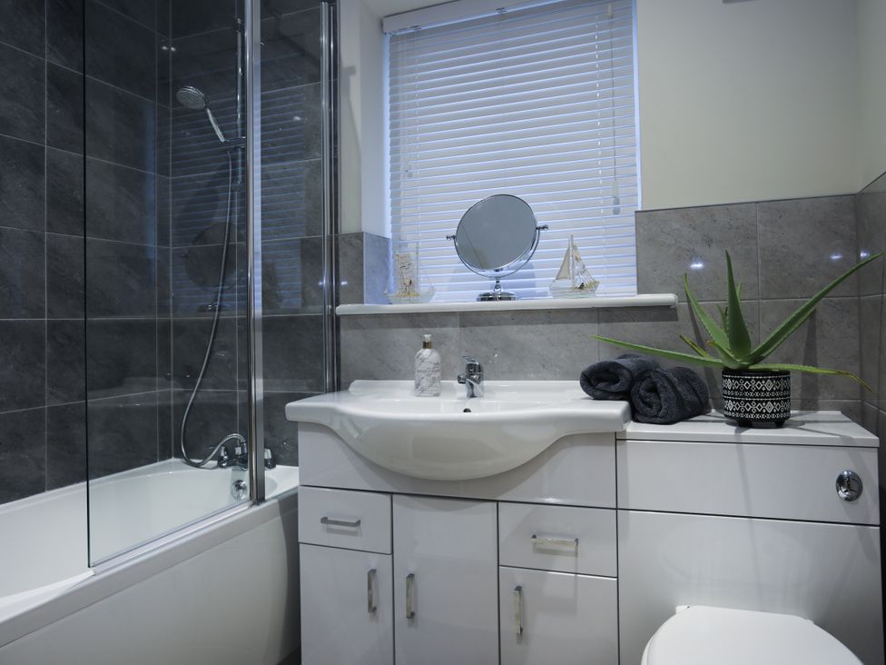 A bathroom with a shower, bathtub, vanity, mirror, and plant at Apartment 3 in Trearddur Bay