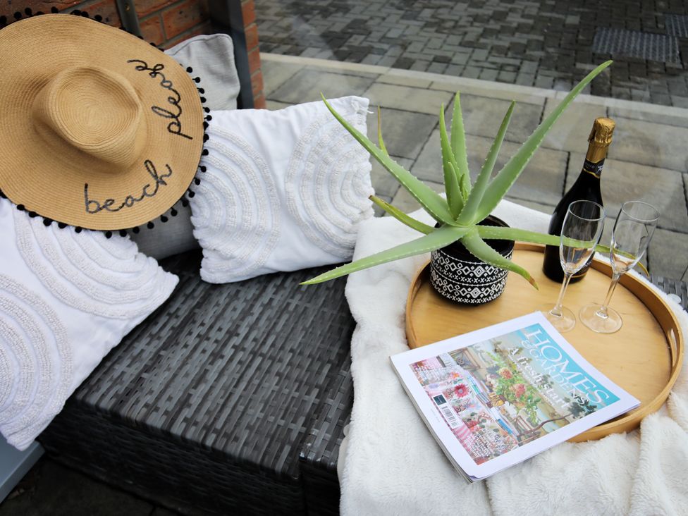 An outdoor seating area with a hat, cushions, plant, tray, champagne bottle, and glasses at Apartment 3 in Trearddur Bay