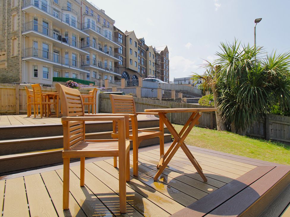 A garden area with wooden furniture and buildings in the background at 11 Cove View Apartments Ilfracombe