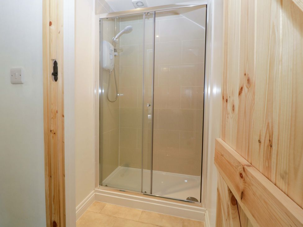 A shower with glass doors and tiles at Redstart Cottage in Kingsland