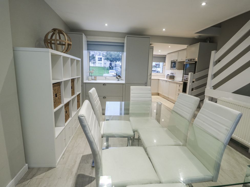 A dining room with a glass table and white chairs at White Sails Y Felinheli